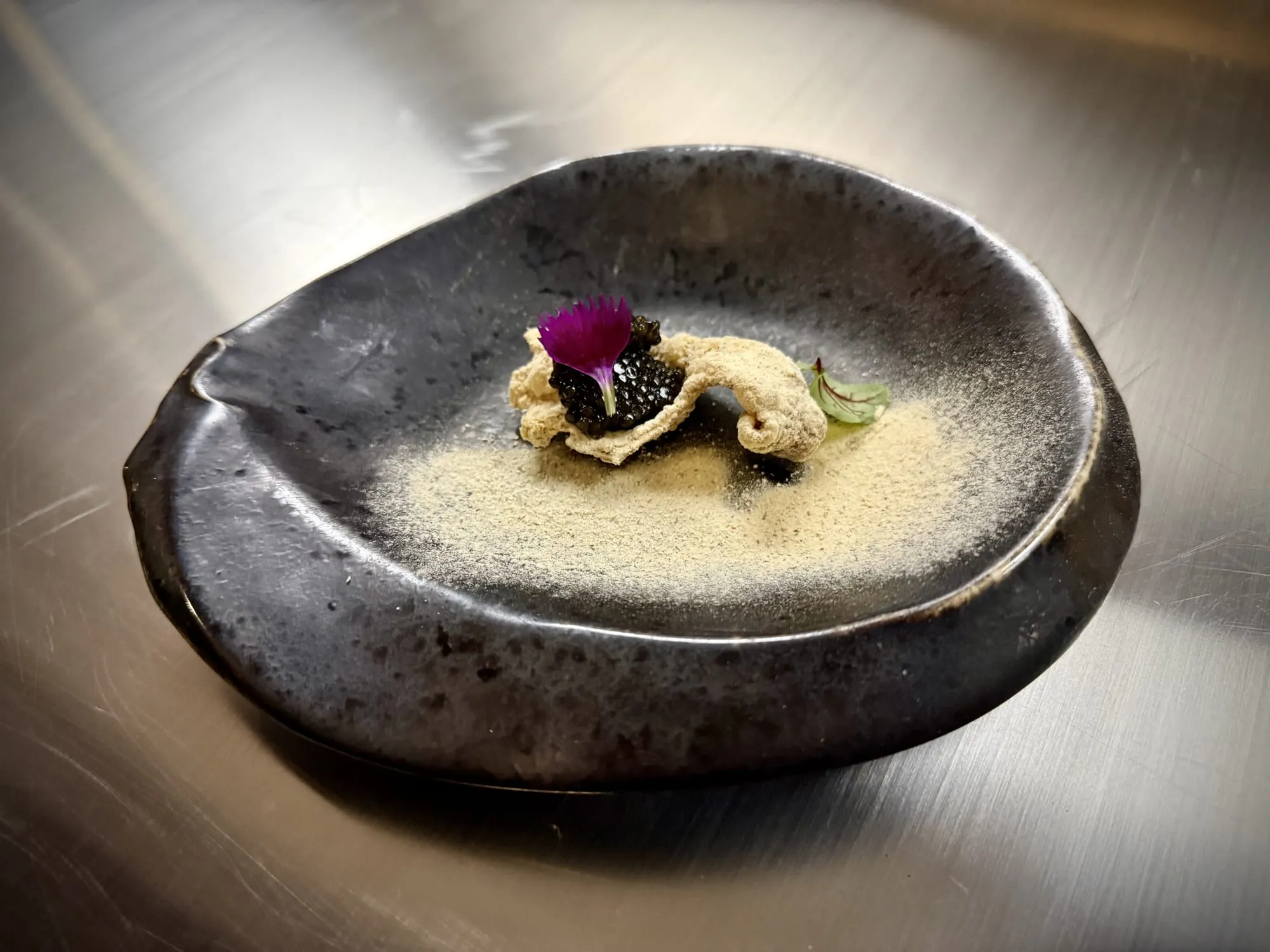 Caviar on crisp chicken skin with a flower petal, on dark ceramic