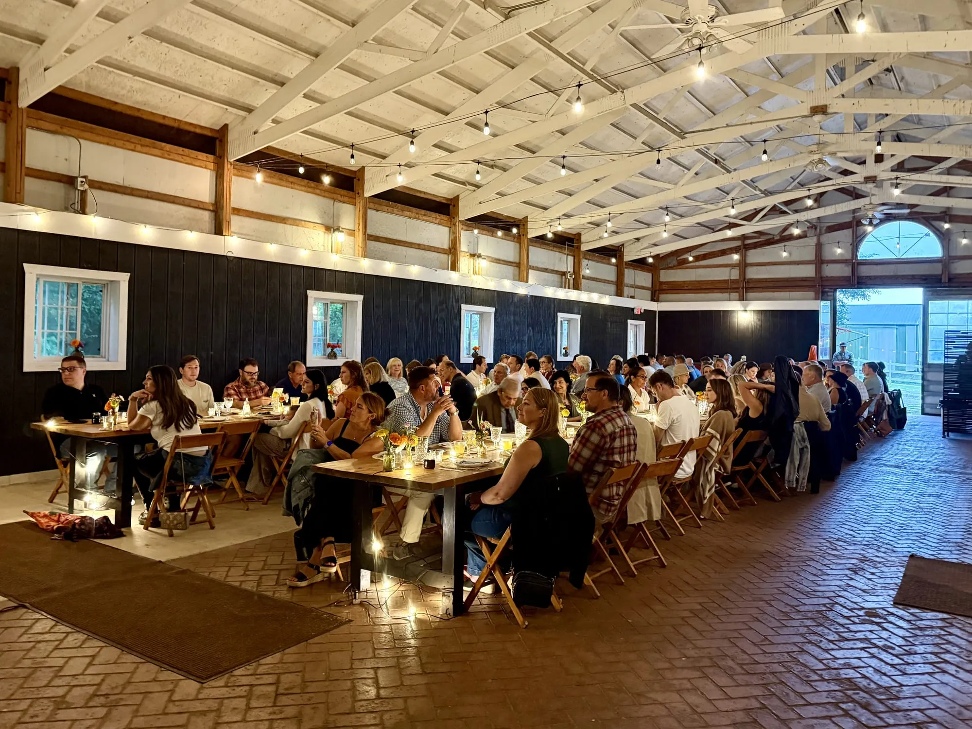 Guests down one long table in the barn at Locavore Farm, string lights on