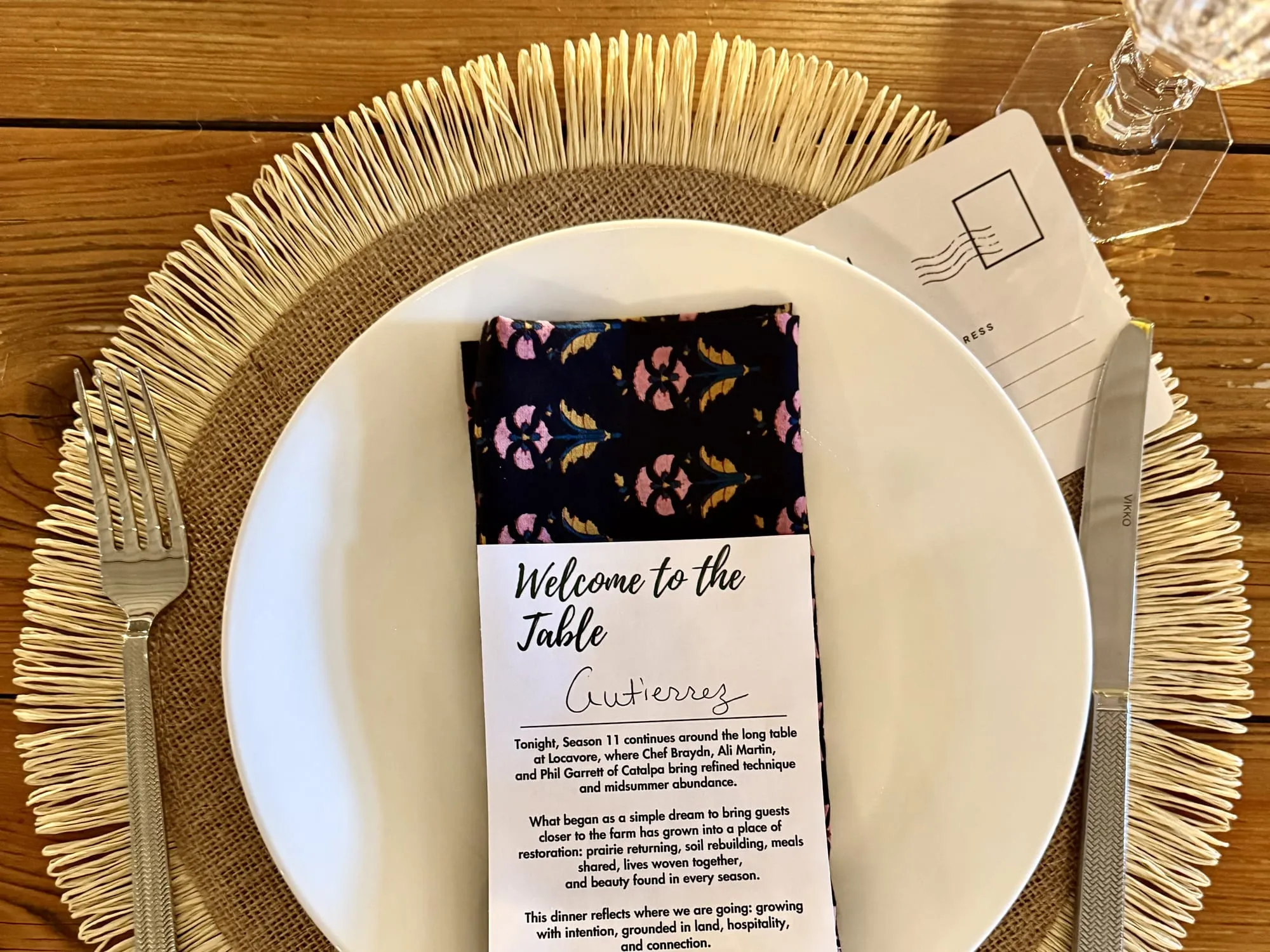 A place setting with a welcome card, block-print napkin, and postcard on a burlap charger