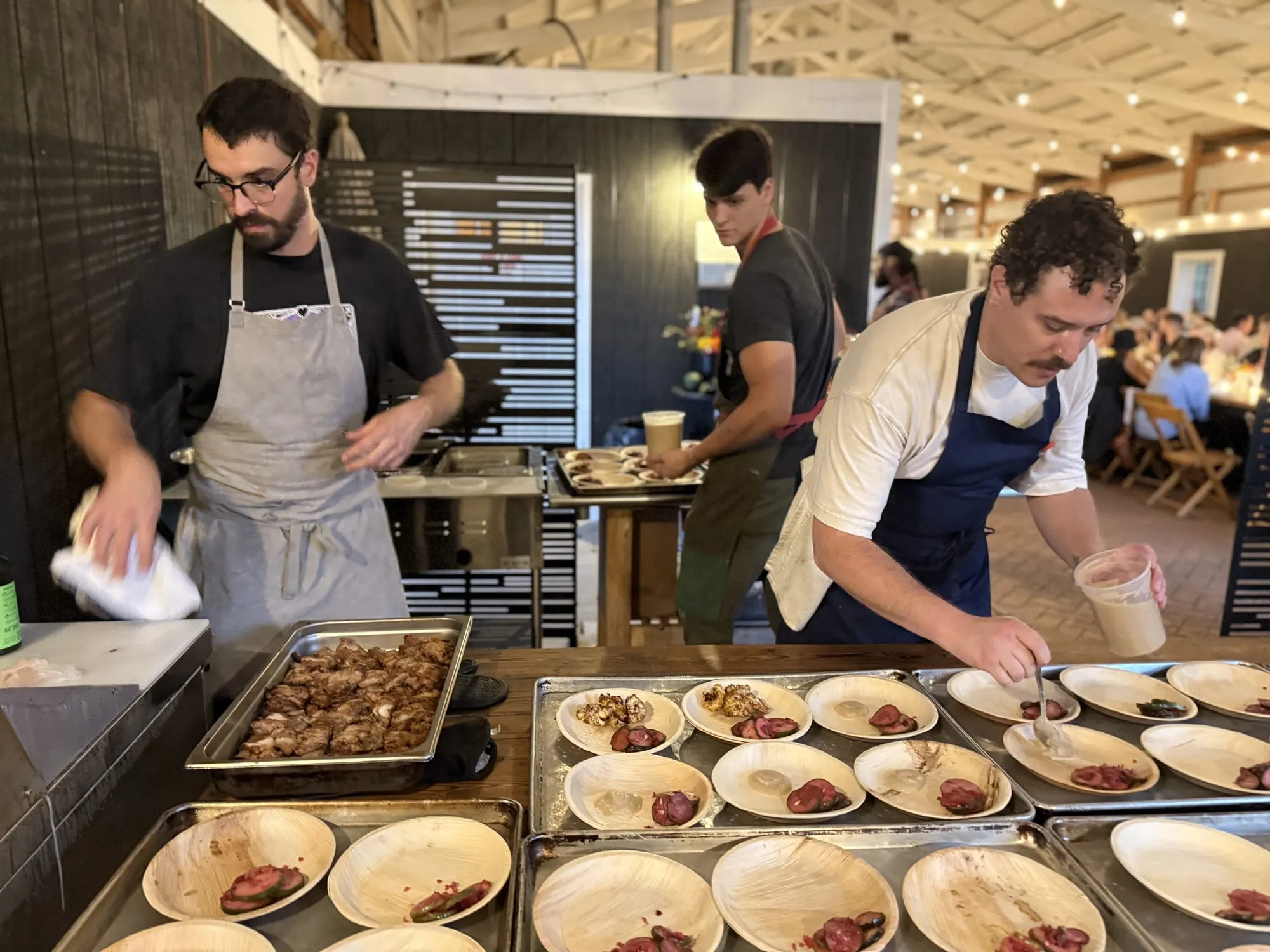 Bradyn and the crew plating a course at the barn pass, guests at the long table behind