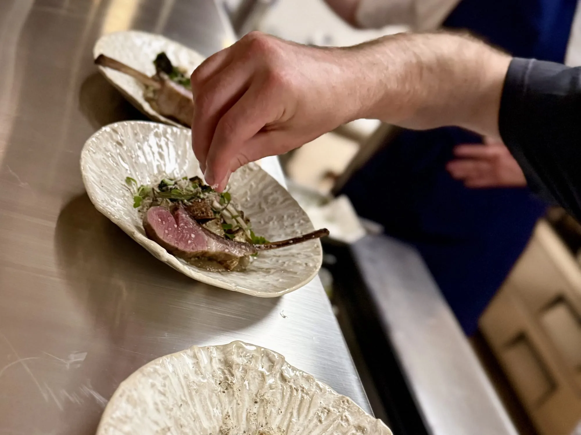 A hand finishing plated lamb chops at the pass of a home dinner